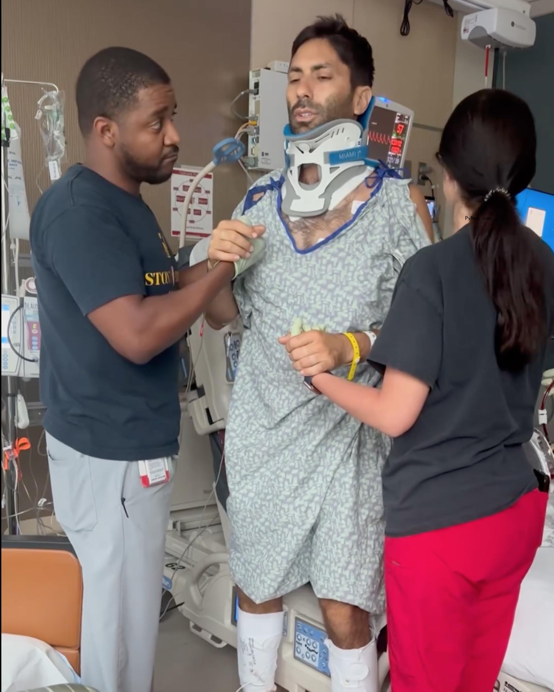 Nev Schulman attempting to stand with the help of two nurses.