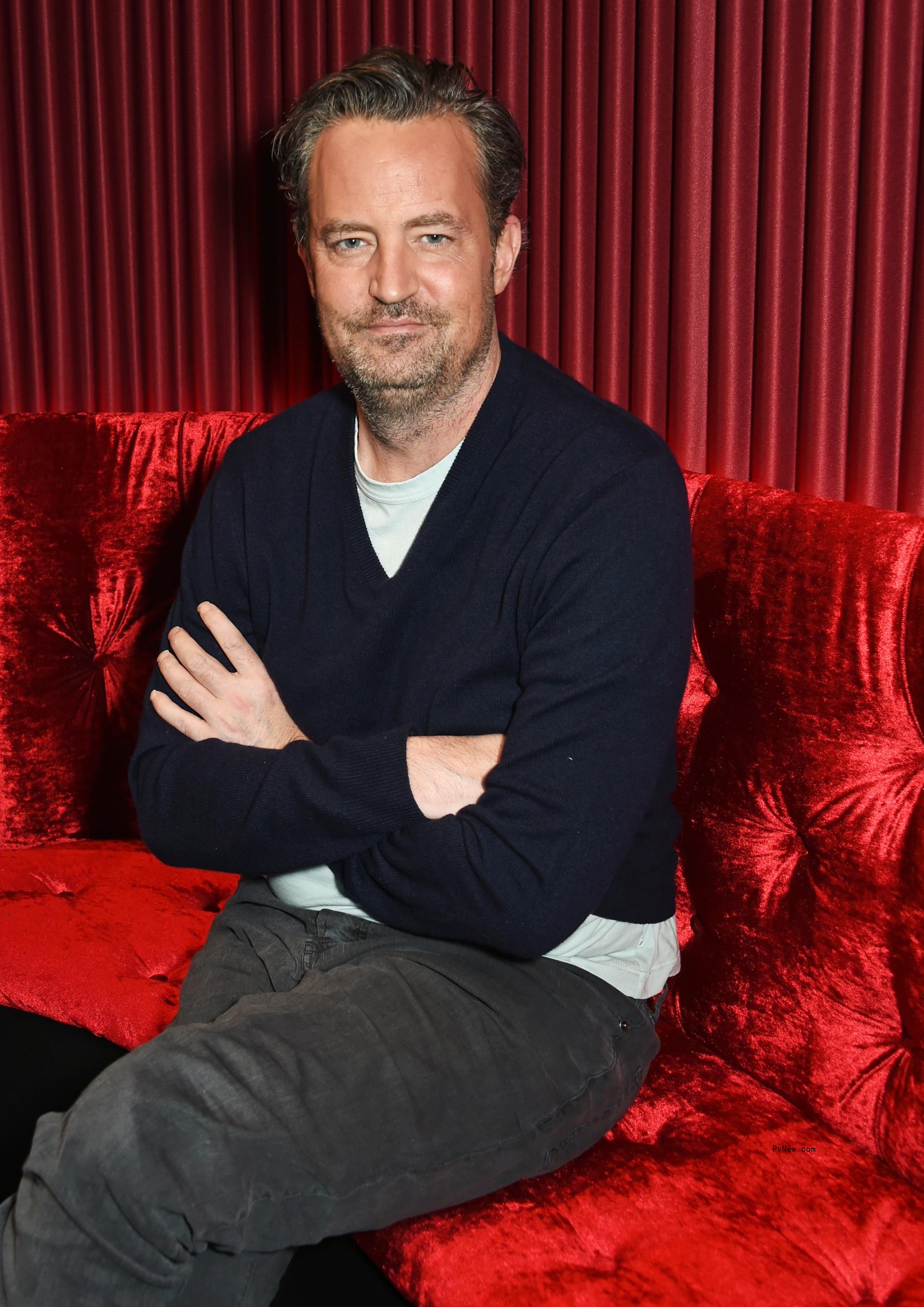 matthew perry sitting with his arms crossed and smiling